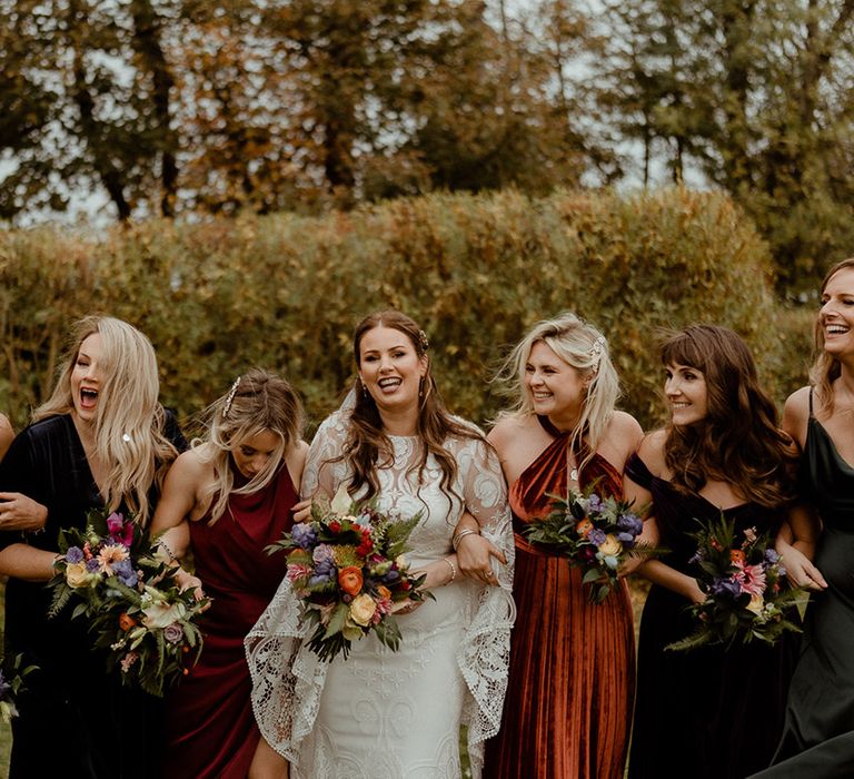 Bridesmaids in mismatched bridesmaid dresses with the bride laughing at the autumnal wedding 