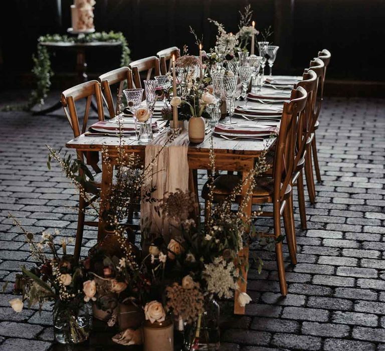 Rustic luxe wedding tablescape at Elmley Nature Reserve wedding venue with white cloth table runners, foliage, baby's-breath, eucalyptus and dried flower floral arrangements, neutral tapered candles and small ceramic vases 