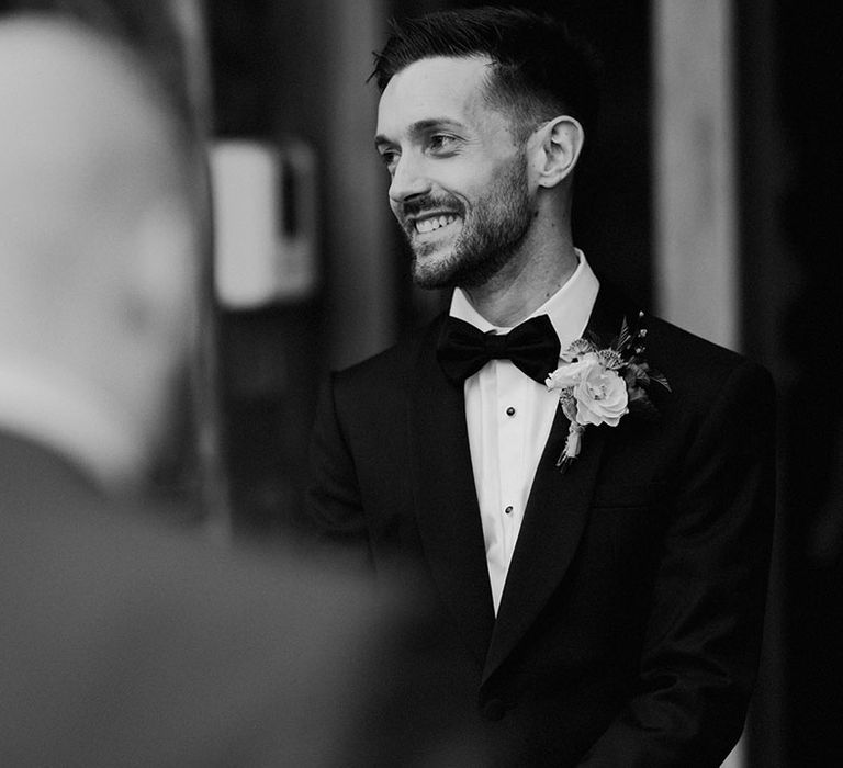 The groom getting dressed into his smart tuxedo with a simple floral buttonhole 