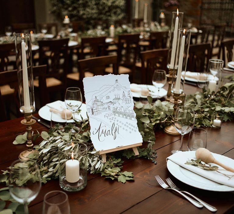 'Amalfi' table name with eucalyptus and tapered white candles at wedding breakfast