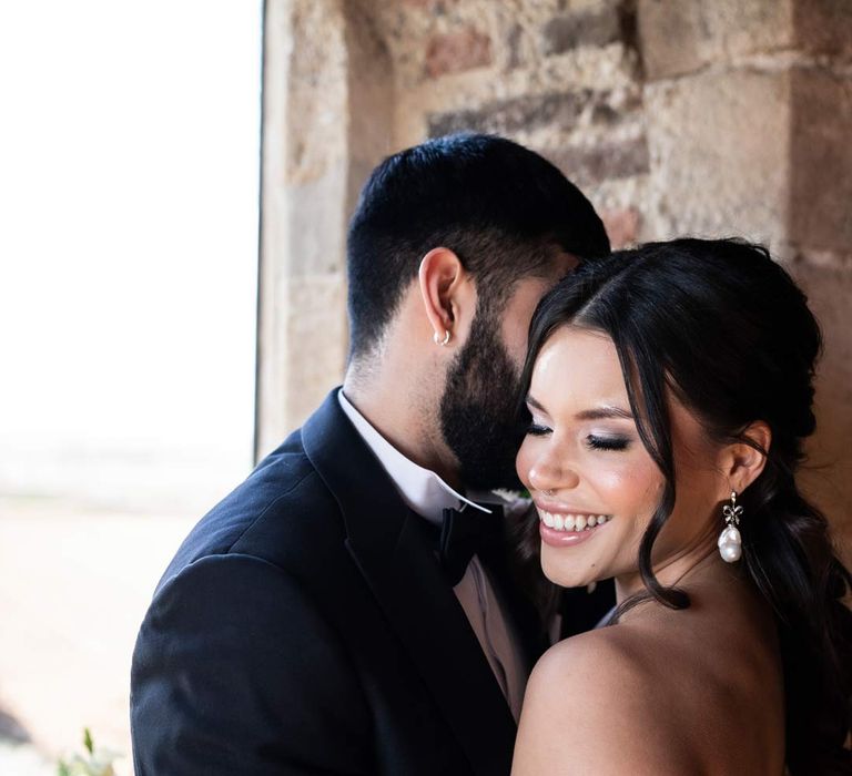 Bride in puddle train ethereal off the shoulder wedding dress with detachable puff tulle sleeves smiling and laughing with groom in classic black tuxedo at Pentney Abbey wedding