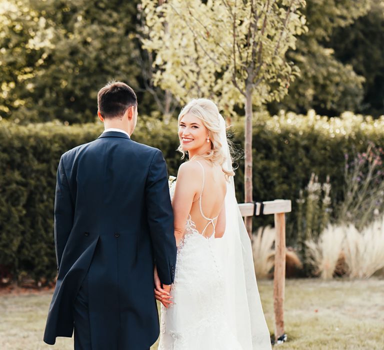 Bride in open back wedding with diamond embellished detail on her wedding dress with mermaid lace skirt walking with the groom 