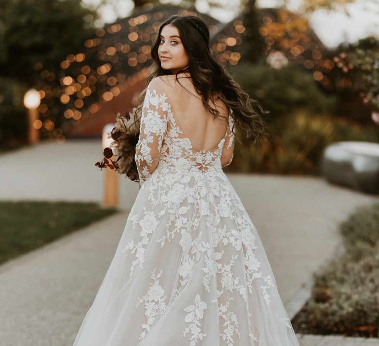 Bride wearing long sleeve lace illusion sleeve wedding dress with overlay holding large autumnal boho dried flower bouquet 