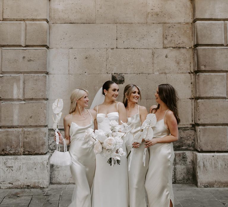 Bridesmaids in white bridesmaid dresses in satin material with white wedding bouquets posing with the bride for modern and minimal city wedding 