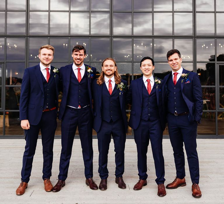 Groomsmen in matching blue three piece suits with red ties, brown shoes, and colourful buttonholes