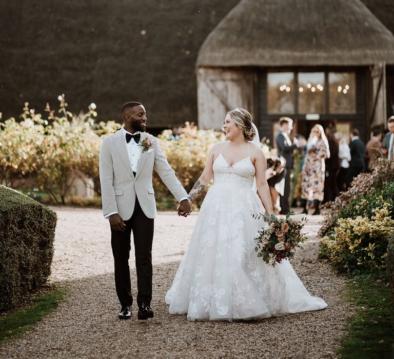 The bride in a princess wedding dress and groom in black tie walk together outside Colville Hall wedding venue 