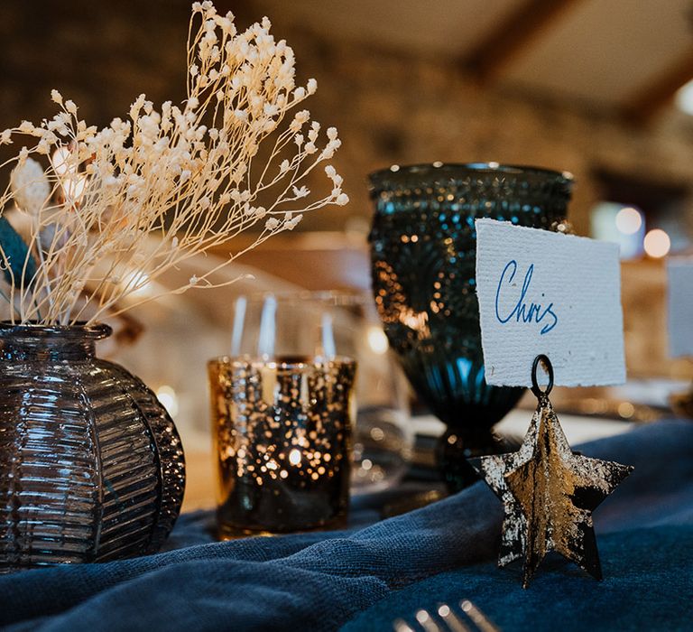 Gold star holdes for the place names with dark blue glassware, table runner and other table decorations 