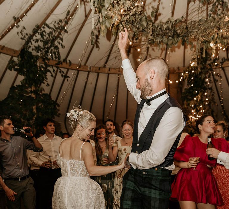 Bride in floral wedding dress with groom in green checkered trousers and black waistcoat having their first dance together 