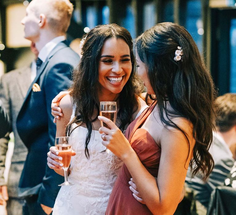 Bridesmaid in cinnamon one shoulder bridesmaid dress embracing bride in a-line tulle wedding dress with beaded lace applique with petals and a square neckline with side tulle cutouts at South Farm wedding