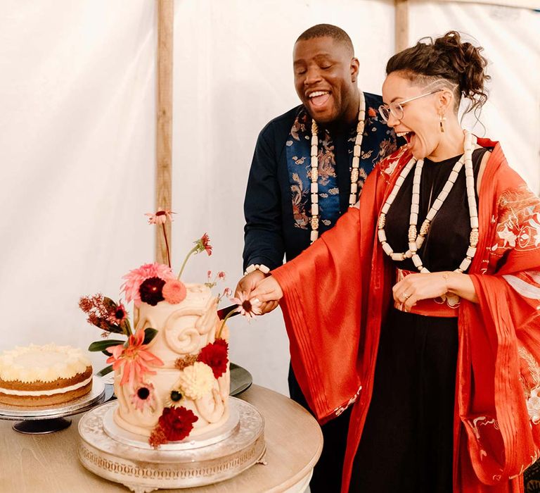 Bride in traditional Chinese wedding kimono standing with groom in navy wedding suit cutting the cake at Broadfield Court