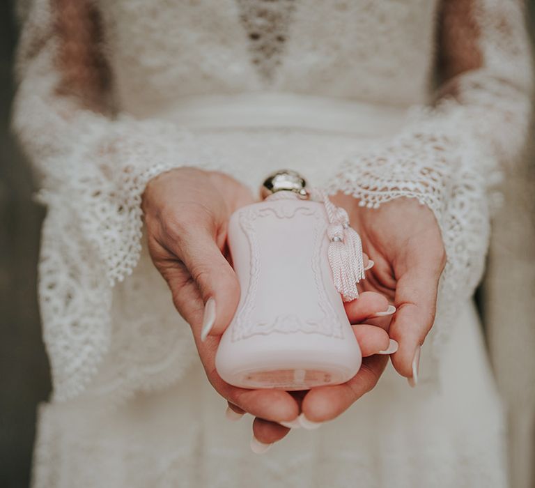 bride with lace bell sleeves holding a pink perfume bottle