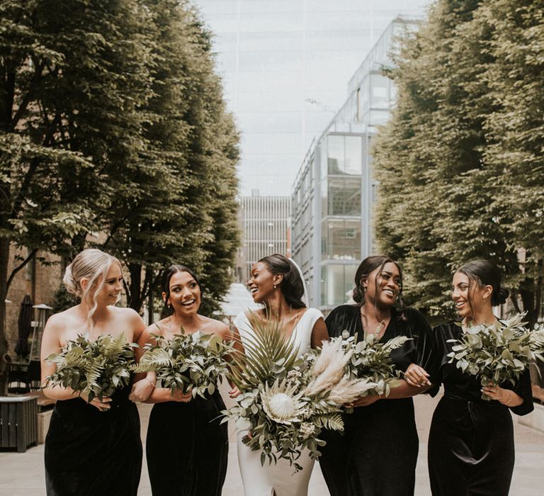 Bride with bridesmaids in black bridesmaid dresses with leafy foliage wedding bouquets