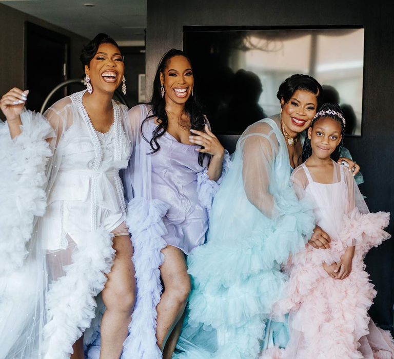 Bride in white sheer tulle and pearl bridal getting ready robe with bridesmaids and flower girl in mismatched pastel sheer tulle and pearl bridal getting ready robes