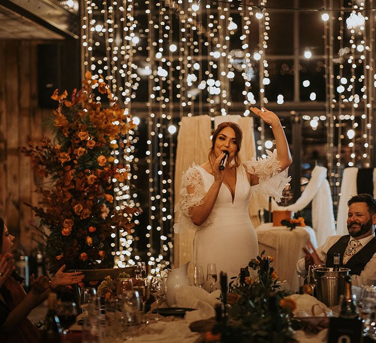 The bride stands up to read out a speech from her phone at the wedding 