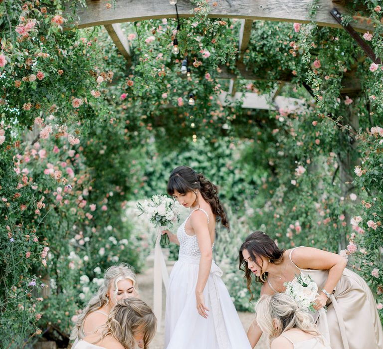 bridal party in champagne gold bridesmaid dresses adjusting the brides wedding train in her Made With Love wedding dress