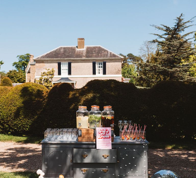 Outdoor wedding reception with a drinks station and hydration station on a vintage dresser 