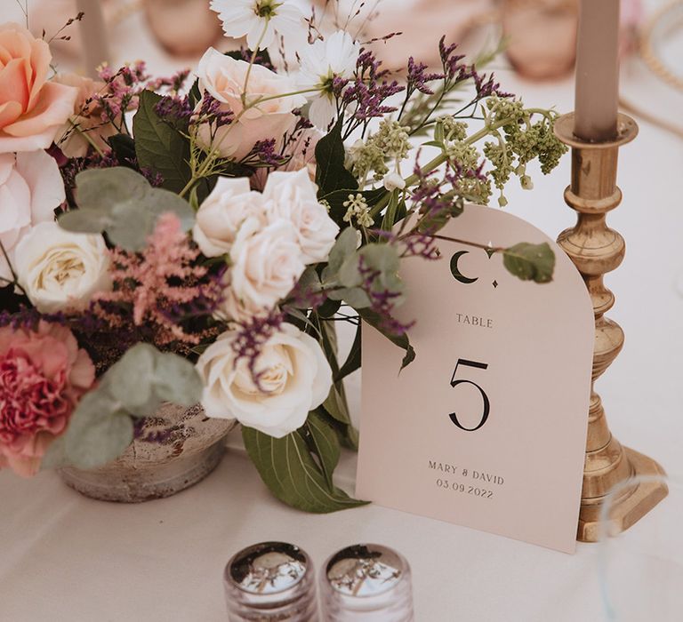 Neutral wedding table number sign next to pink wedding flower arrangements on the table 