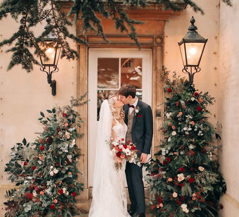 Bride wearing intricate embroidered wedding veil and lace wedding dress in front of red wedding flower decorations 