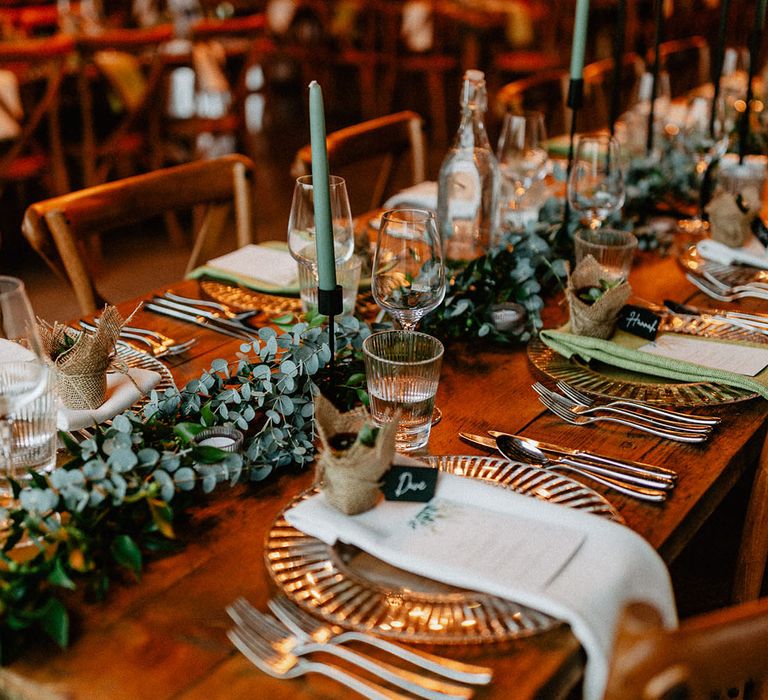 Rustic barn wedding venue with tables decorated with eucalyptus table runner, green taper candles and more on wooden tables 