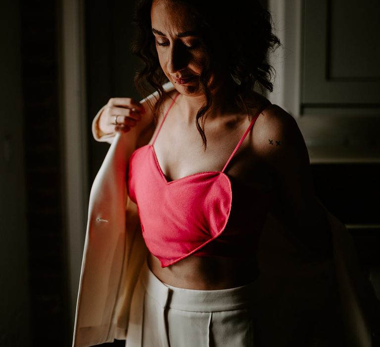 Bride wearing a pink heart shaped top putting on her white blazer over the top 