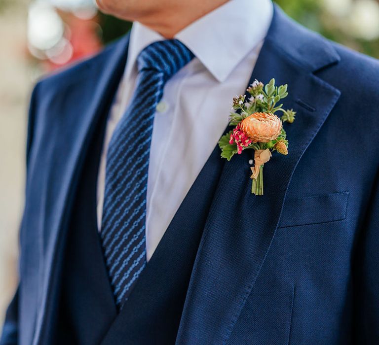 Groom wearing blue wedding suit with colourful flower buttonhole 