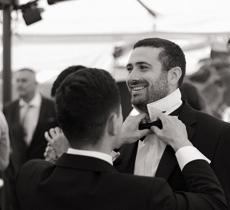 Groomsman helps the groom put on the bow tie for the wedding 