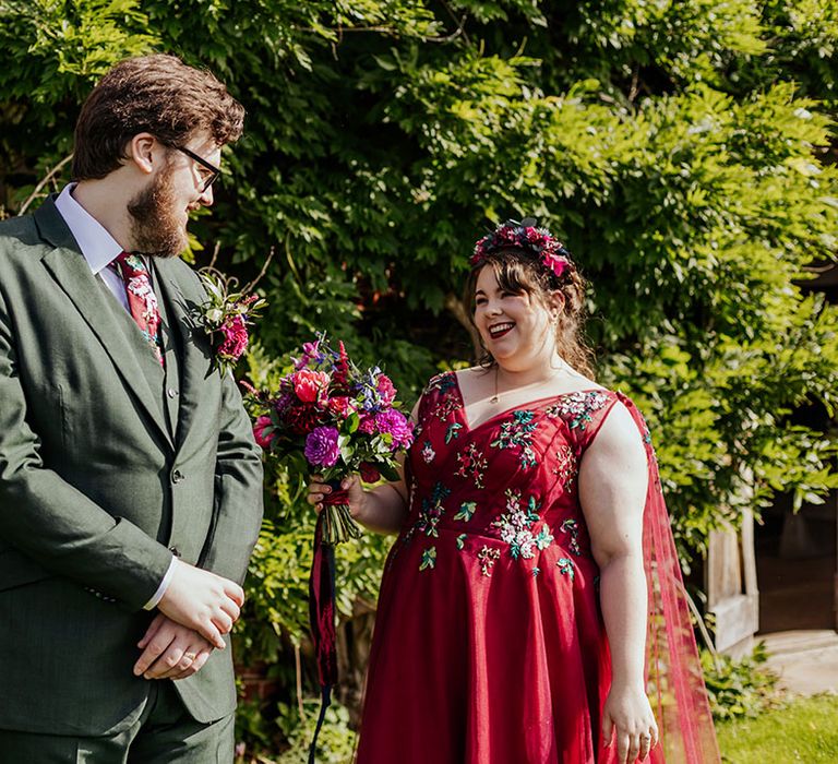 First look between bride and groom before their wedding ceremony with the groom wearing a green suit and red floral embroidered wedding dress