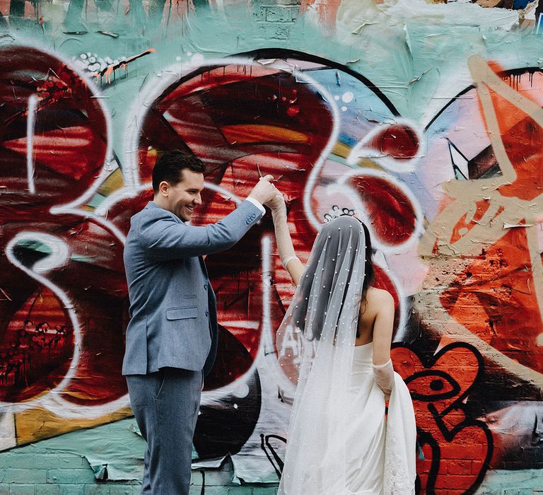 The groom in a light blue wedding suit spins the bride around for their cute couple portrait moment 