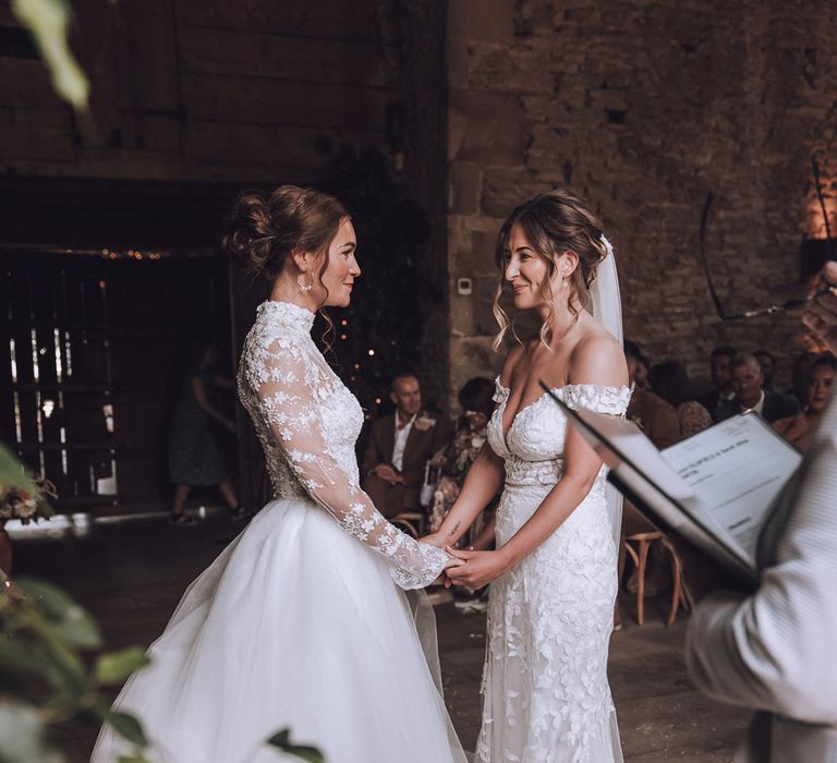 Bride in high neck long sleeve flower wedding dress facing bride in off the shoulder wedding dress at their same sex wedding 