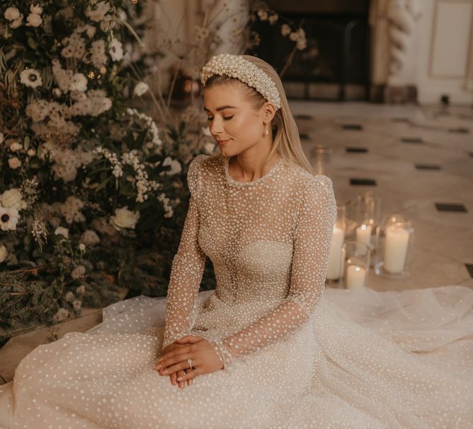 Bride in sparkly wedding dress and pearl headband sitting on the floor 