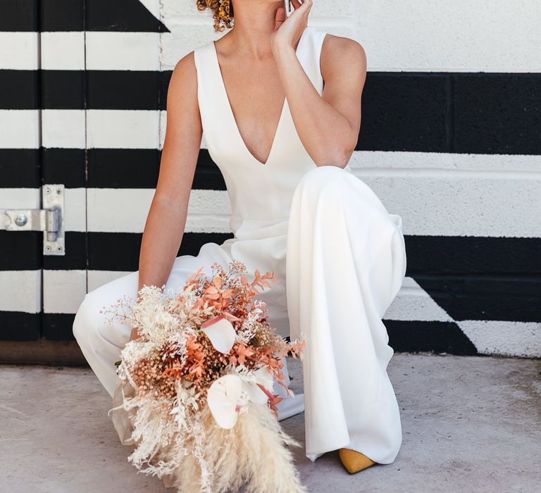 Stylish bride with naturally curly hear wearing a white jumpsuit 