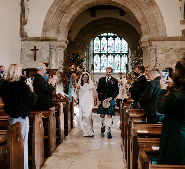 Bride and groom celebrate as they exit the church. Behind them are Chritsmas church wedding flowers