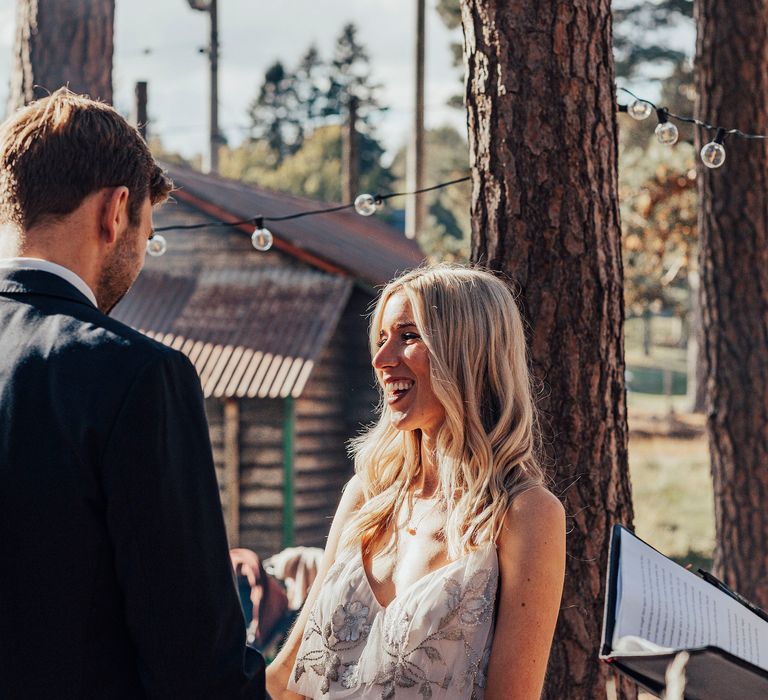 Blonde bride laughs during woodland wedding ceremony