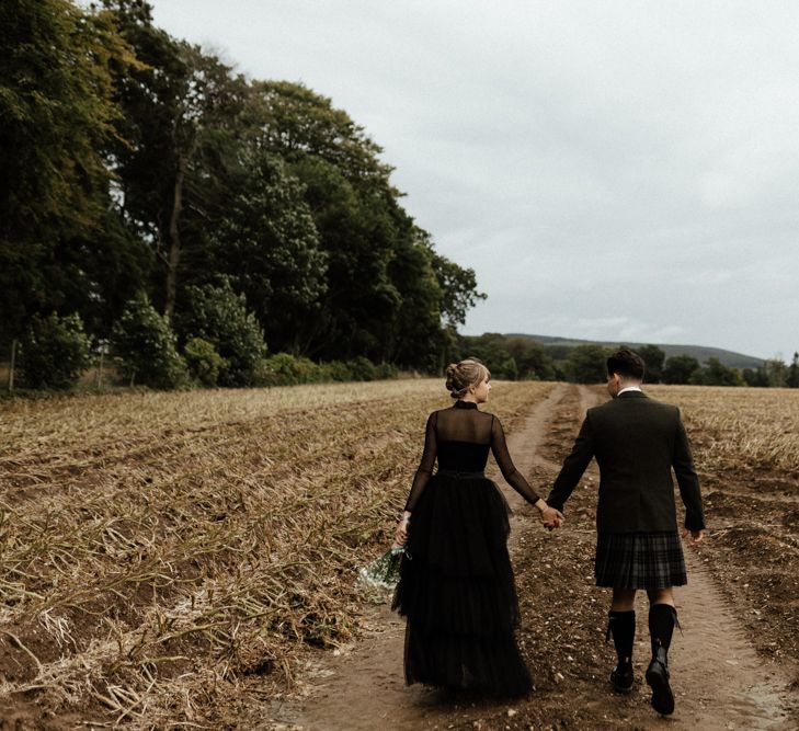 Bride & groom holds hands whilst walking through fields