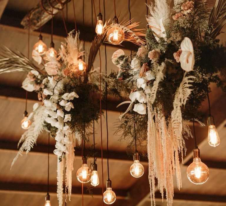 Hanging installation with festoon lights and boho wedding flowers including anthuriums and dried grasses 