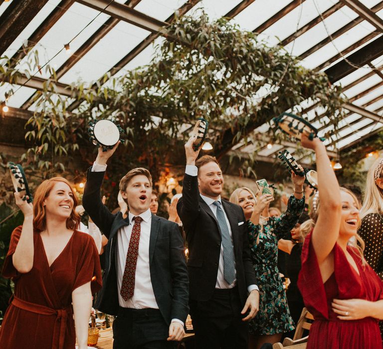 Wedding guests waving their personalised tambourine wedding favours during the autumn themed wedding 