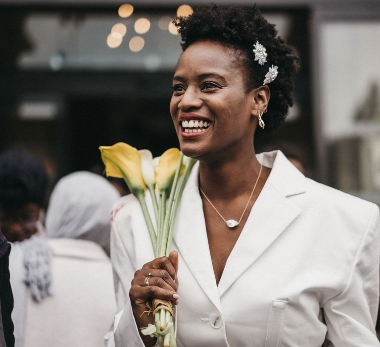 West African bride with short hair in a blazer dress holding yellow lilies 