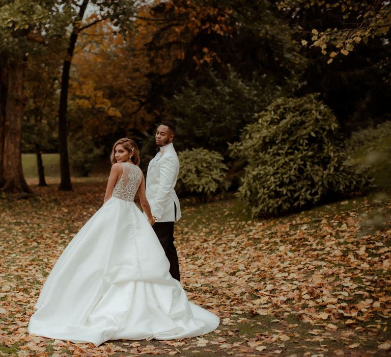 Portrait of the bride in an embellished back wedding dress with buttons holding her grooms hand in a white tuxedo jacket 