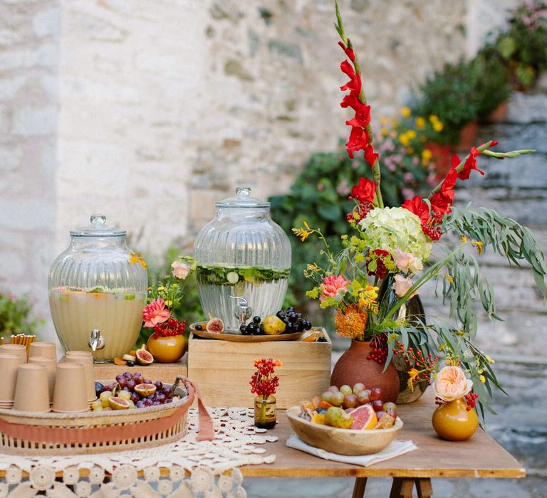 A small grazing table with fruit, fresh water and lemonade, with red and green flower decorations