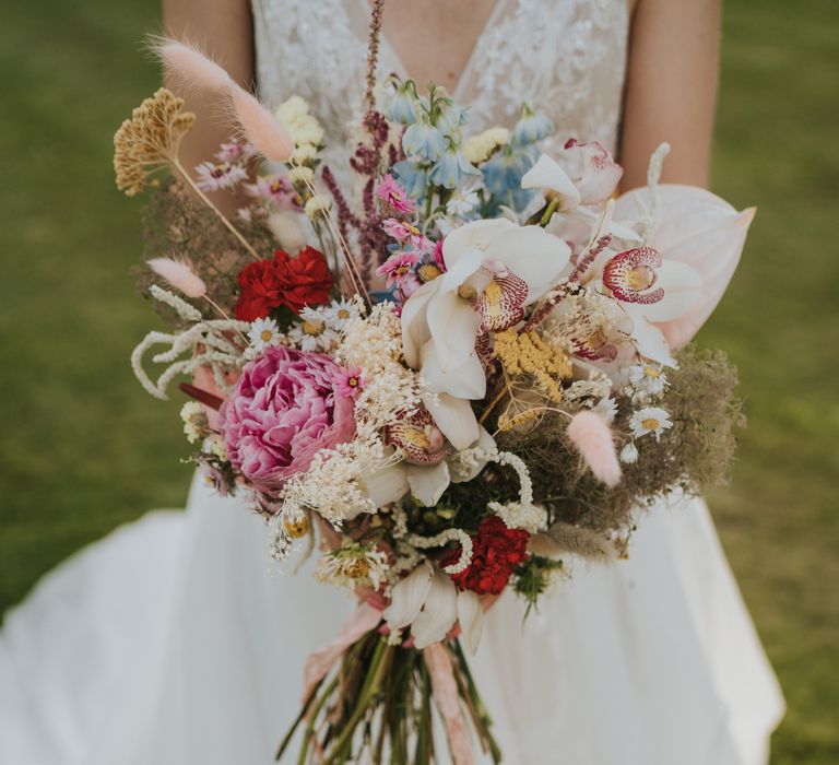 Bride holds out colourful bouquet which is tied with silk pastel pink ribbon