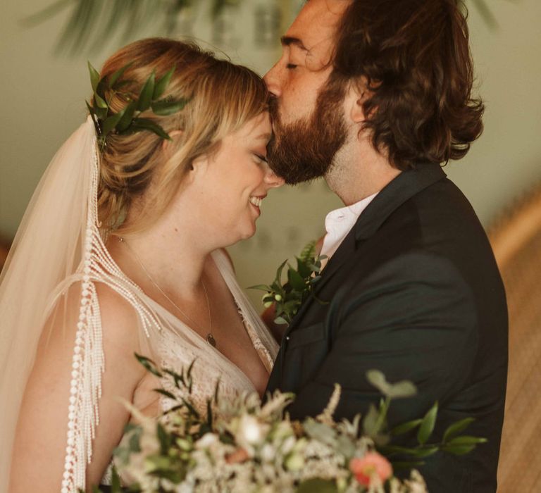 Groom kisses bride on the forehead during botanical wedding