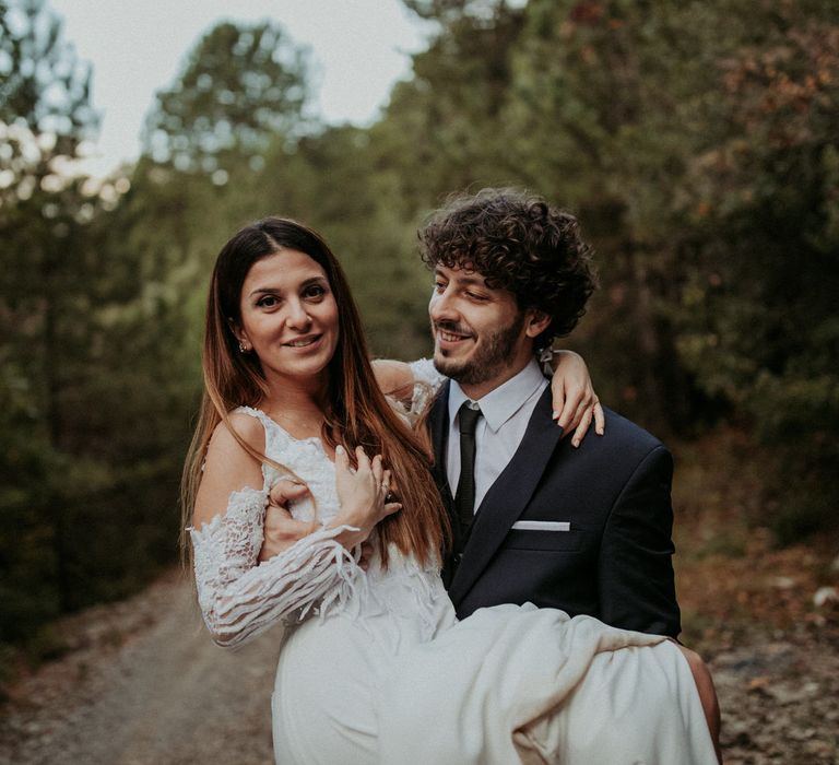 The groom lifting the bride in his arms along a woodland road