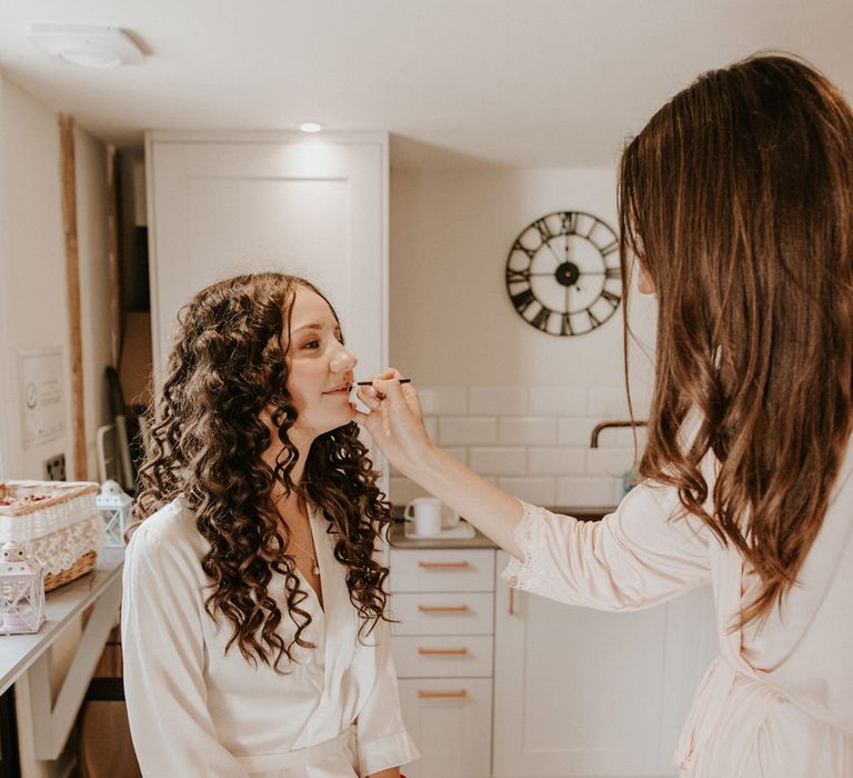 Bride with long wavy hair having her makeup done on the wedding morning 