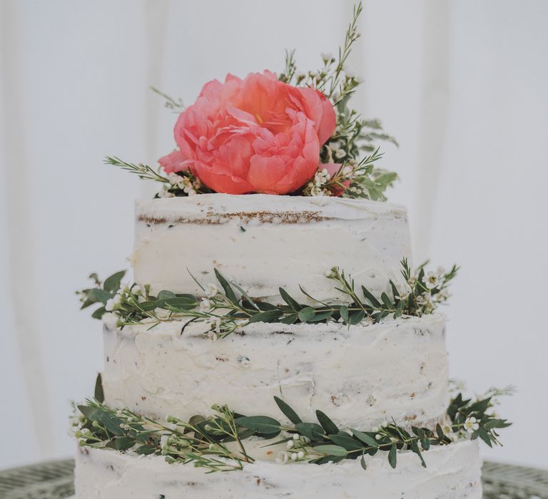 Naked white wedding cake with pink floral decor and green foliage