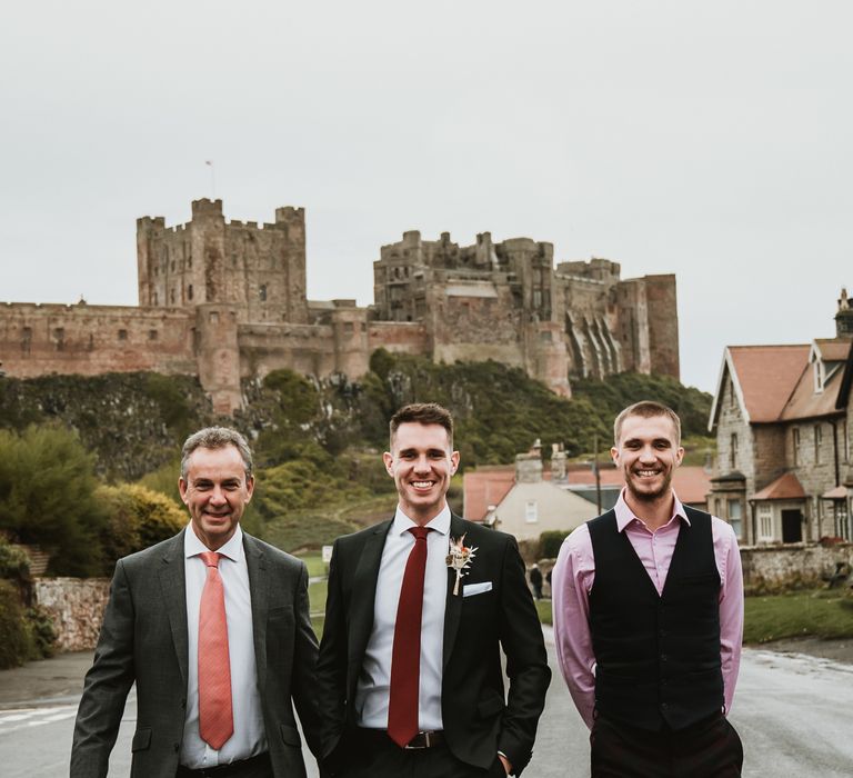 Groom and groomsmen walk together with Bamburgh Castle in the background