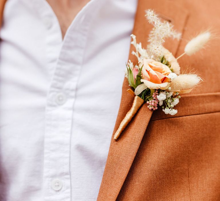 Groom in a white shirt and rust blazer with small orange buttonhole flower