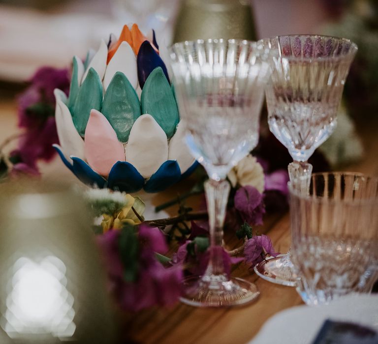 Multicoloured ceramic artichoke wedding decoration set upon pink floral table garland with crystal wine glasses at enchanted forest wedding