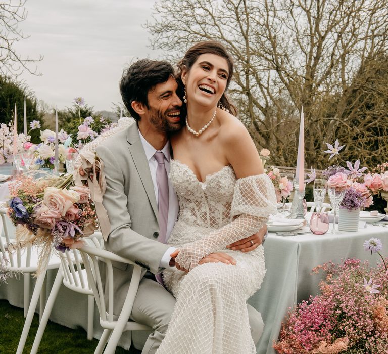 Bride & groom sit together at table whilst bride wears lace gown with long gloved sleeves