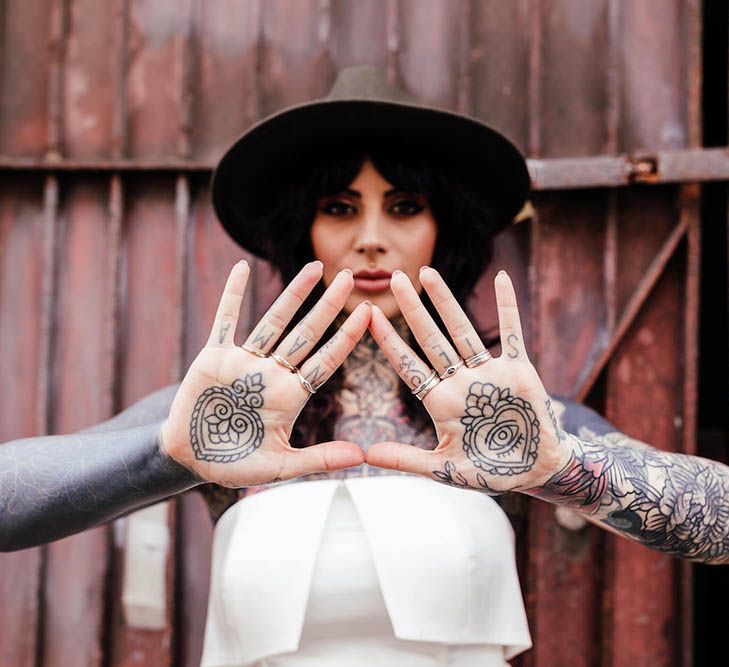 Alternative bride in a strapless wedding dress and fedora hat showing her body art on her hands 