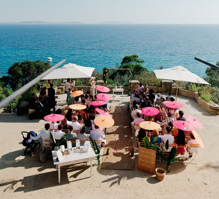 Guests shield from the sun under pink and orange parasols